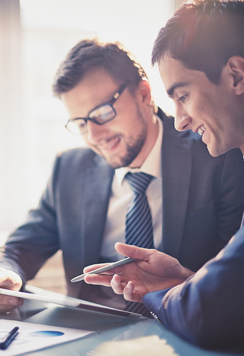 two coworkers lean over a tablet at a meeting